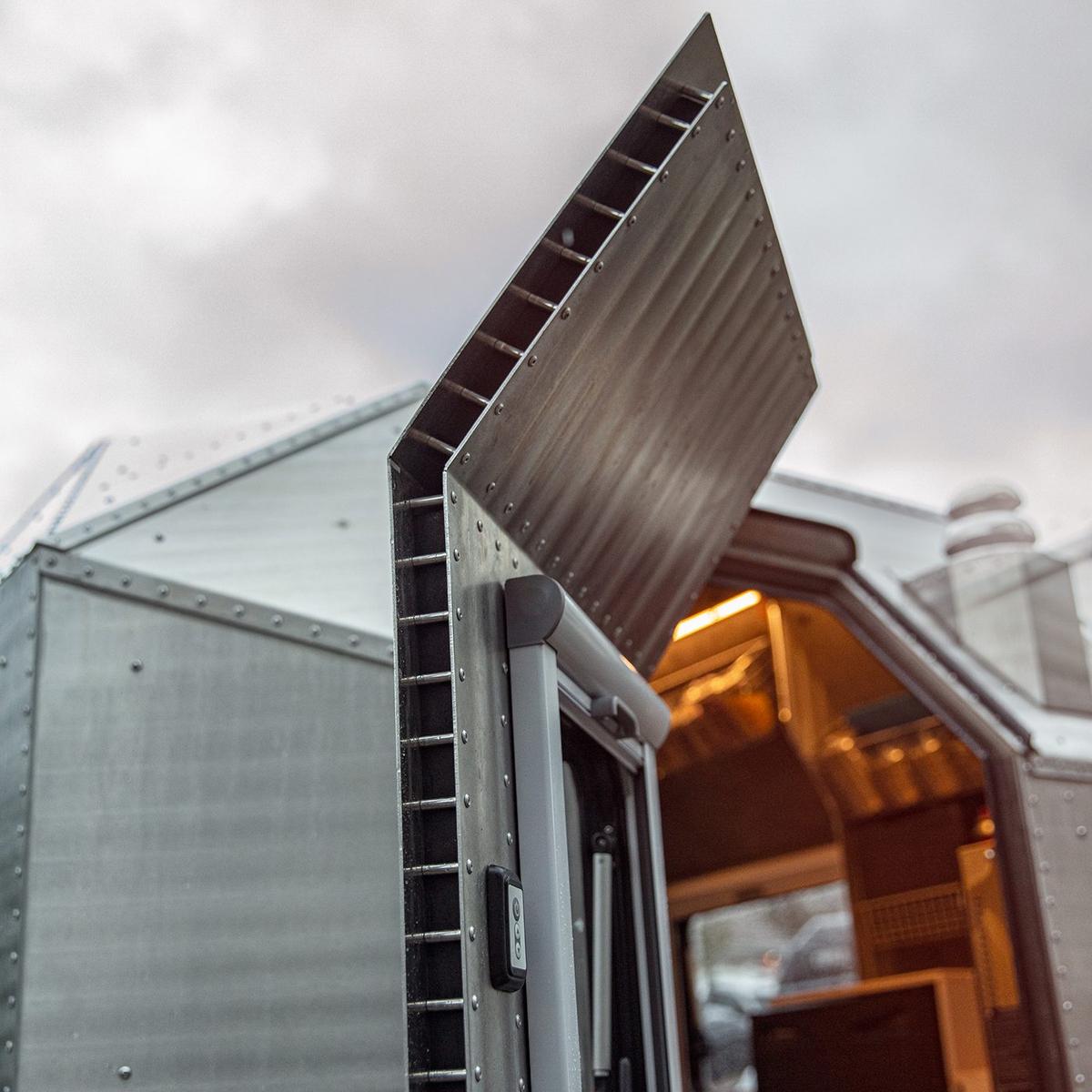 Hand-riveted aluminum side panel of a Kimbo truck bed camper propped open at the Bellingham, Washington workshop, exposing the laser-cut 5052 aluminum panels, solid-rivet pattern, and frameless monocoque construction.